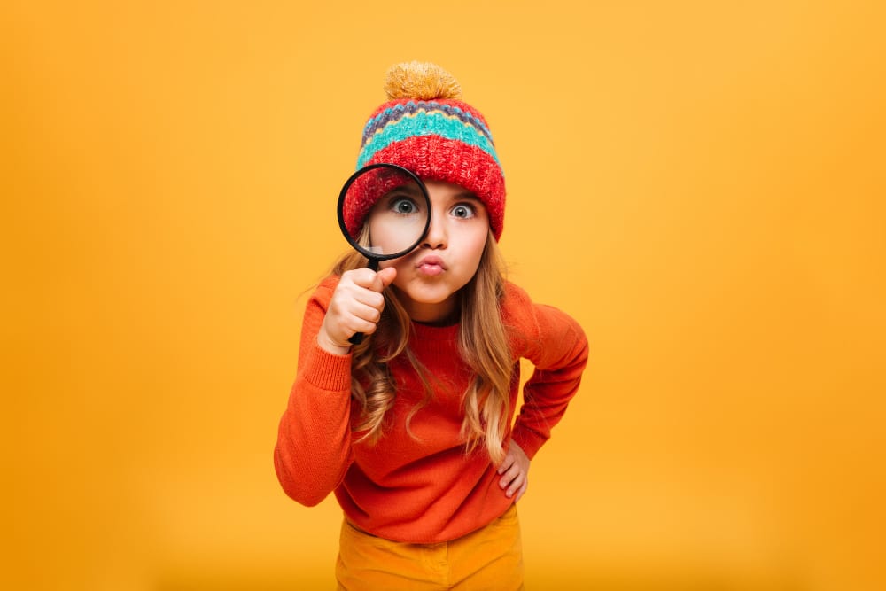 joyful young girl sweater hat looking camera with magnifier orange